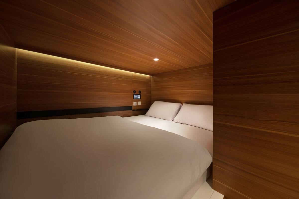 A modern bedroom with a wooden panel wall, a large bed, and a control panel on the wall.