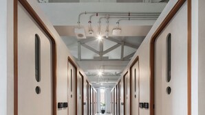 Un pasillo largo y estrecho con puertas de madera y letreros de habitación numeradas, que conduce a una habitación luminosa con un gran ventanal.