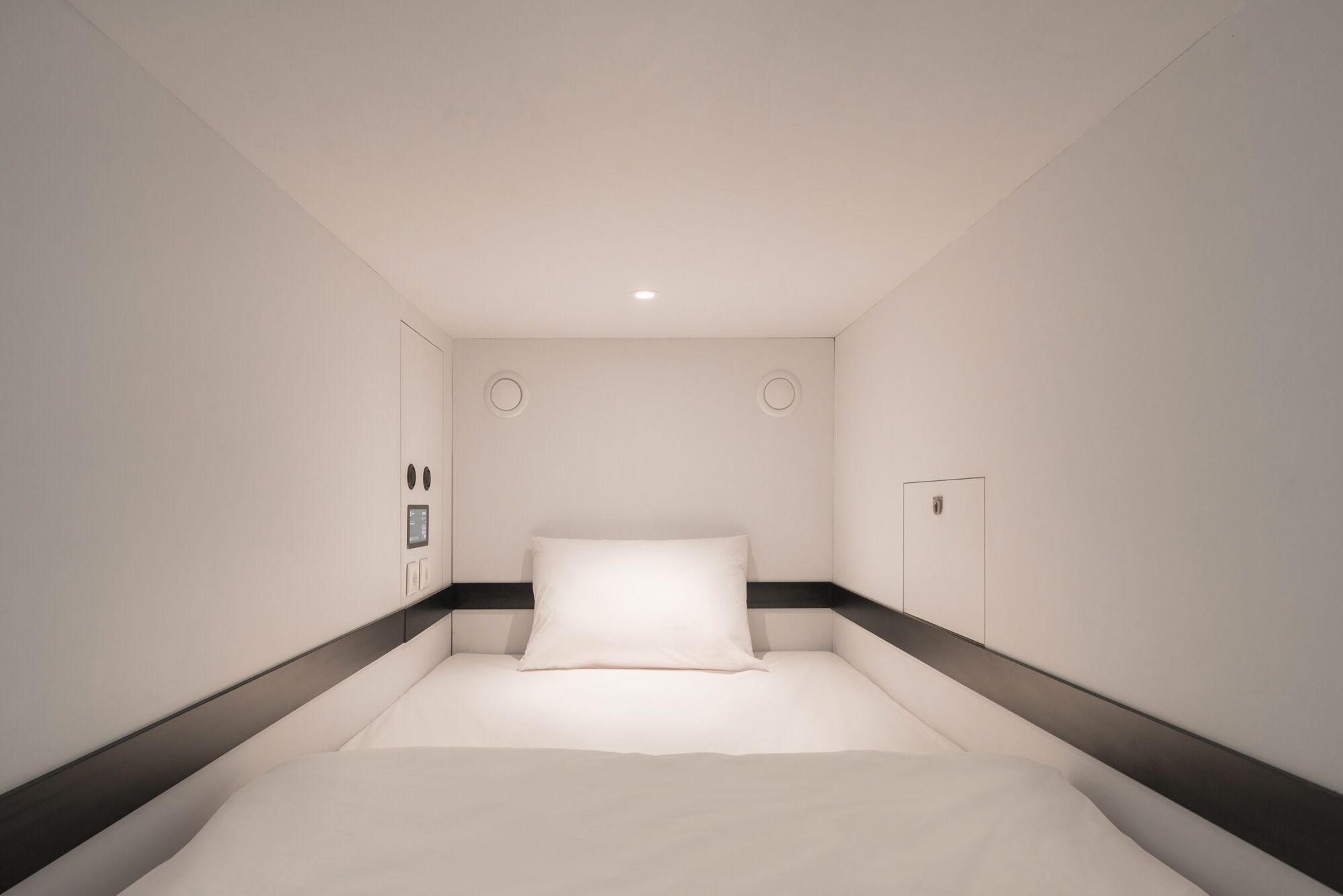 A modern hotel room with a large bed, a control panel, and a door.