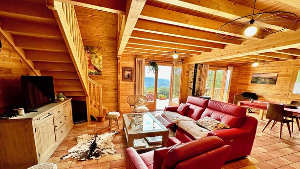 A cozy log cabin interior with a red sofa, wooden dining table, and a television on a cabinet.