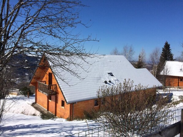 A wooden cabin with a sloped roof, a balcony, and a snow-covered landscape.