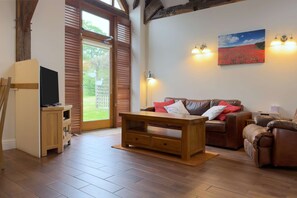 A living room with a wooden floor, a sofa, a TV, a table, and a painting on the wall. - Within the South Downs National Park, 7 miles north of Brighton. (Hassocks)