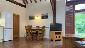 A kitchen with a white refrigerator, wooden dining table with chairs, a television on a wooden stand, and a large window with a view of greenery. - Within the South Downs National Park, 7 miles north of Brighton. (Hassocks)