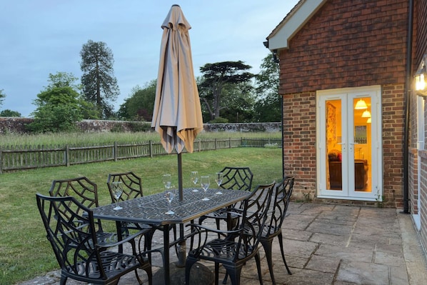 Une terrasse extérieure avec une table et des chaises, un parasol et un bâtiment en briques doté d’une porte.