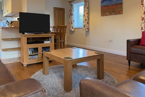Un salon avec une table basse en bois, un canapé en cuir, un meuble pour la télévision et un tableau accroché au mur.