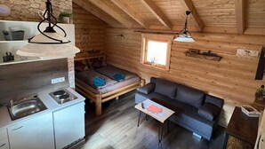 Un intérieur de chalet chaleureux comprenant un coin cuisine, un canapé, une table à manger et une fenêtre laissant entrer la lumière naturelle.