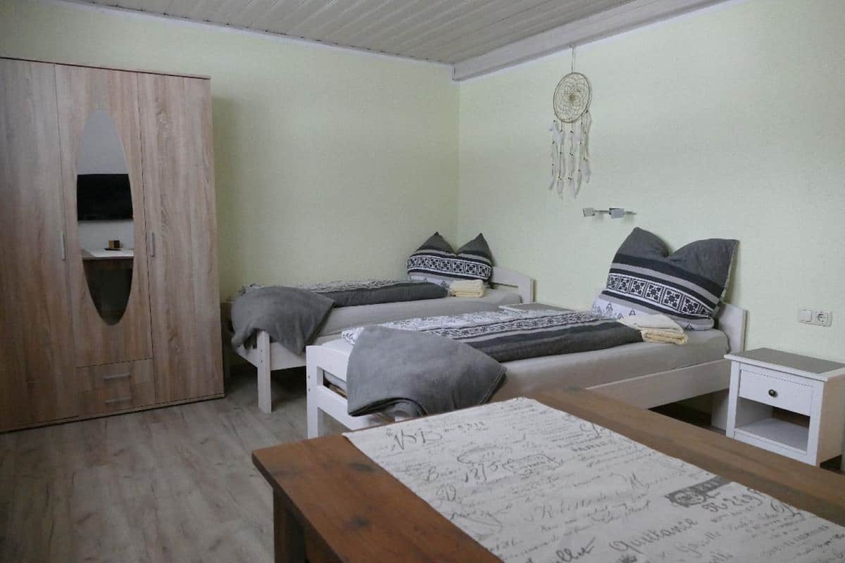 Une chambre avec deux lits, une armoire, une table de chevet et un attrape-rêves accroché au mur.