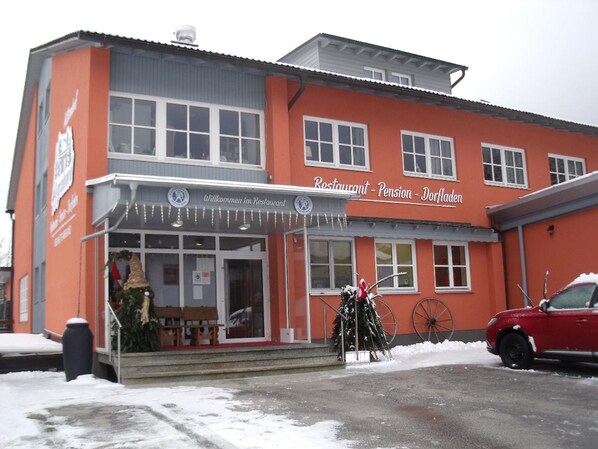 A two-story building with a red facade and a sign that reads "Restaurant - Pension - Dorfladen". - Hüttendorf 49 gradnord (Bayerisch Eisenstein)