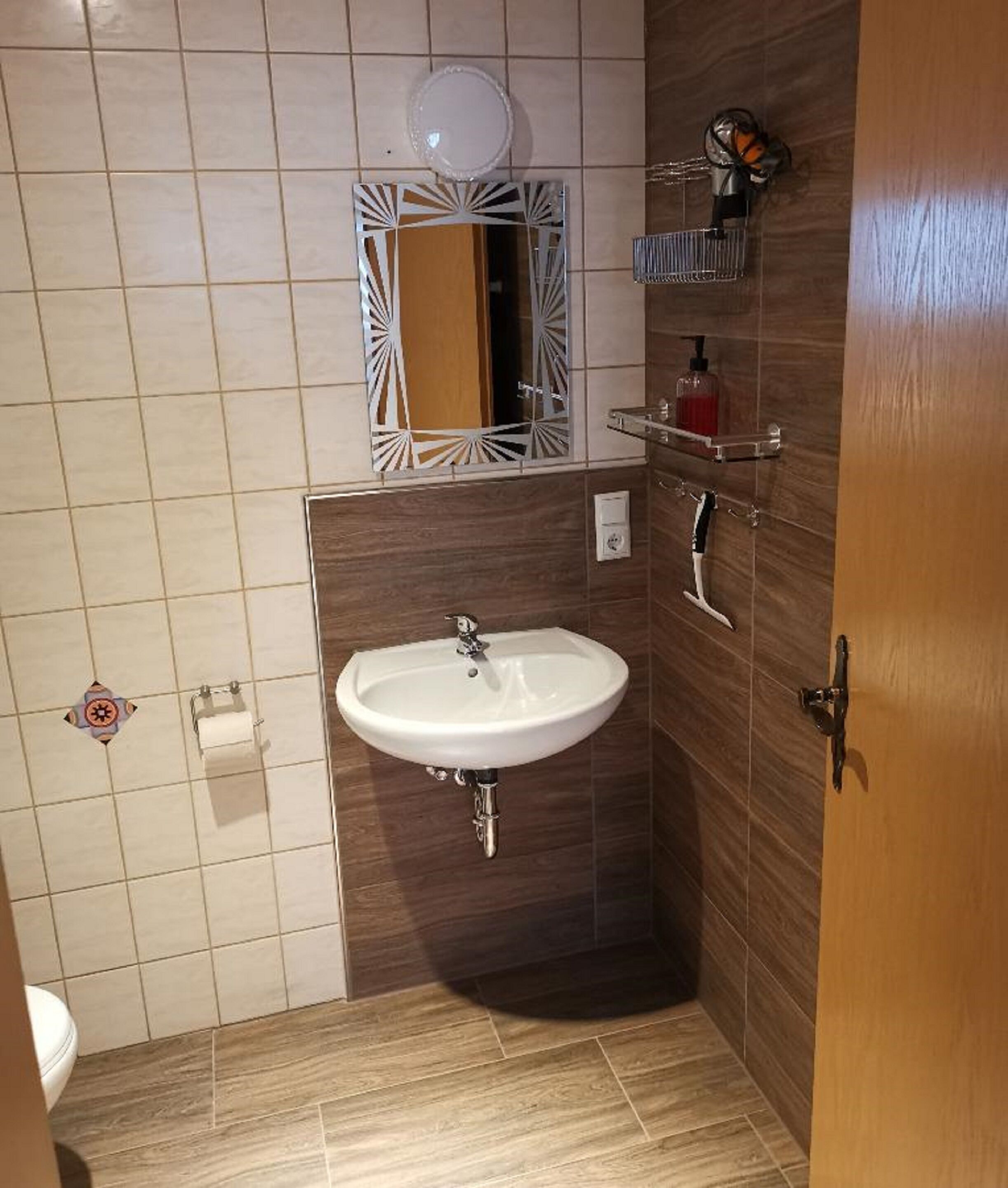 A bathroom with a white sink, a mirror with a decorative frame, a soap dispenser, and a towel rack.