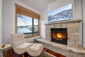Een knus vertrek met een stenen openhaard, een groot raam met uitzicht op een besneeerd landschap en een comfortabele fauteuil.