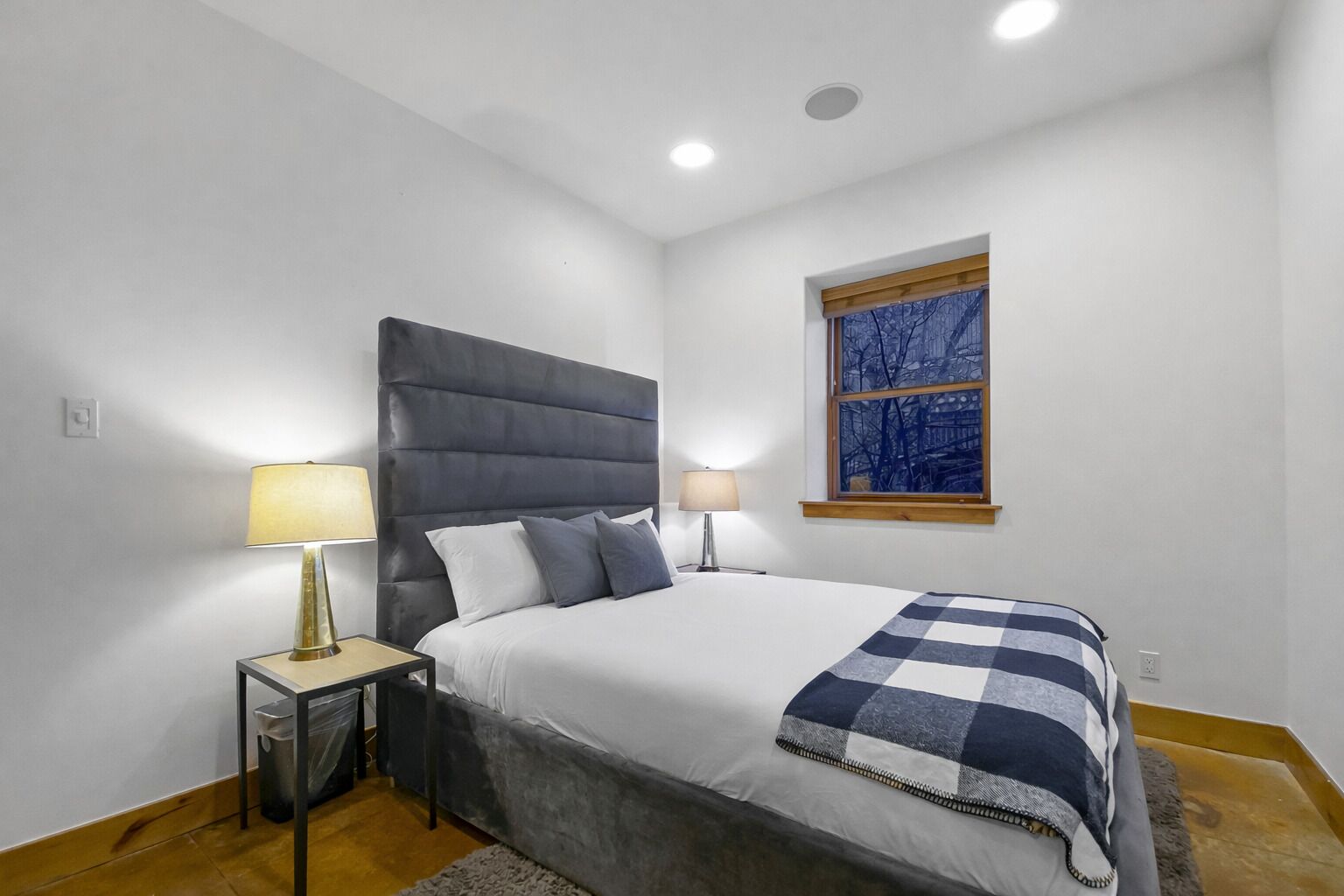 A modern bedroom with a large bed, two bedside tables with lamps, a window with a cityscape view, and a small rug.