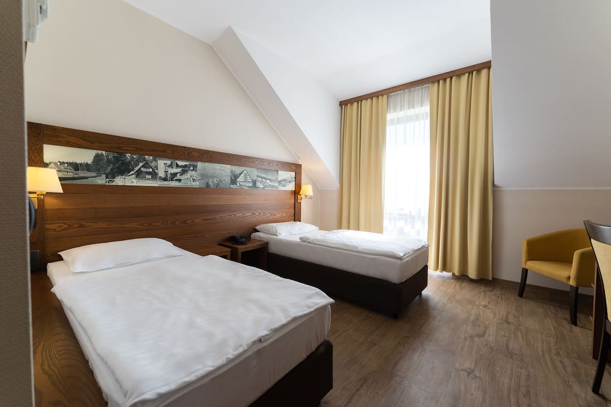 A hotel room with two beds, a wooden headboard with a black and white photo, a yellow chair, and a window with curtains.