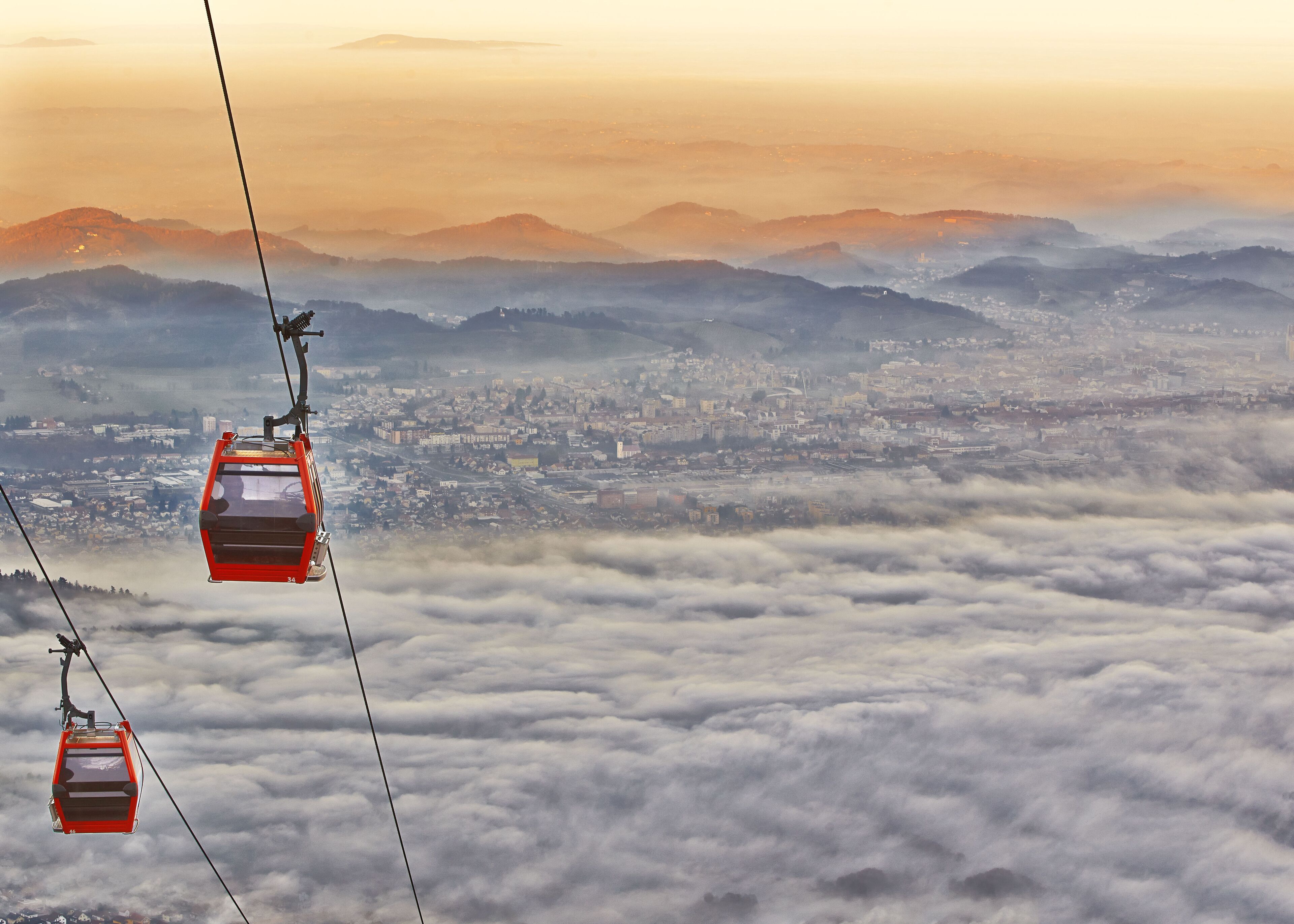 A cable car system over a city with a mountainous backdrop.