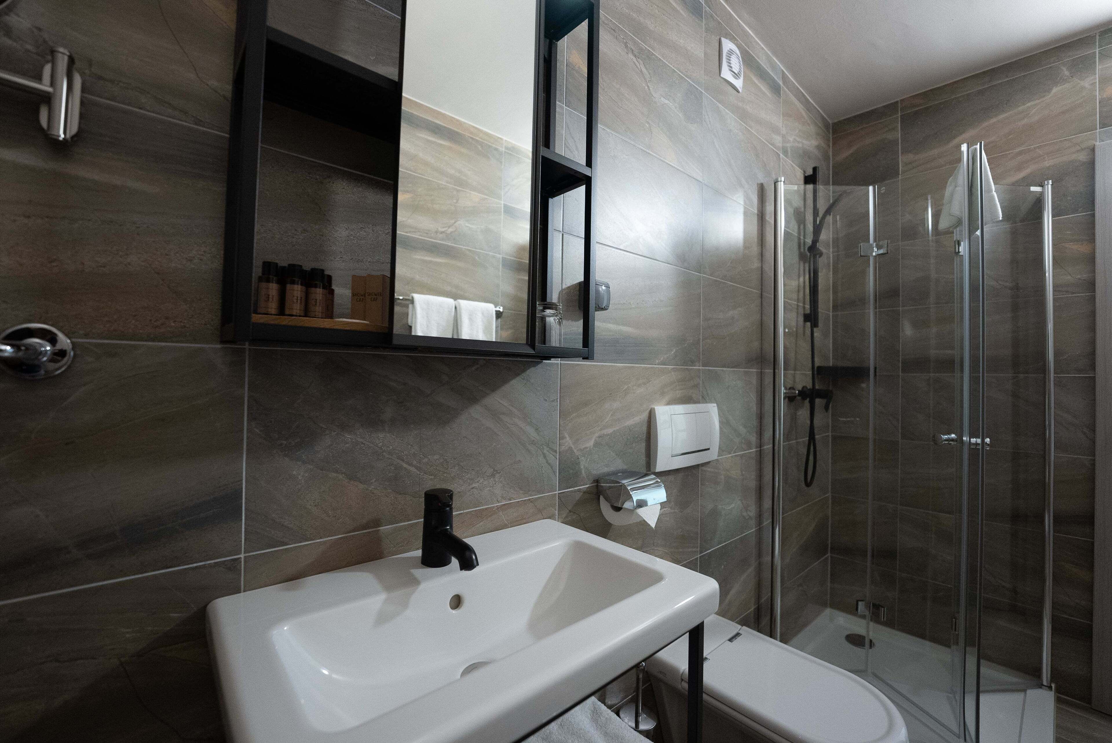 A modern bathroom with a white sink, a mirror, a glass shower enclosure, and a toilet.