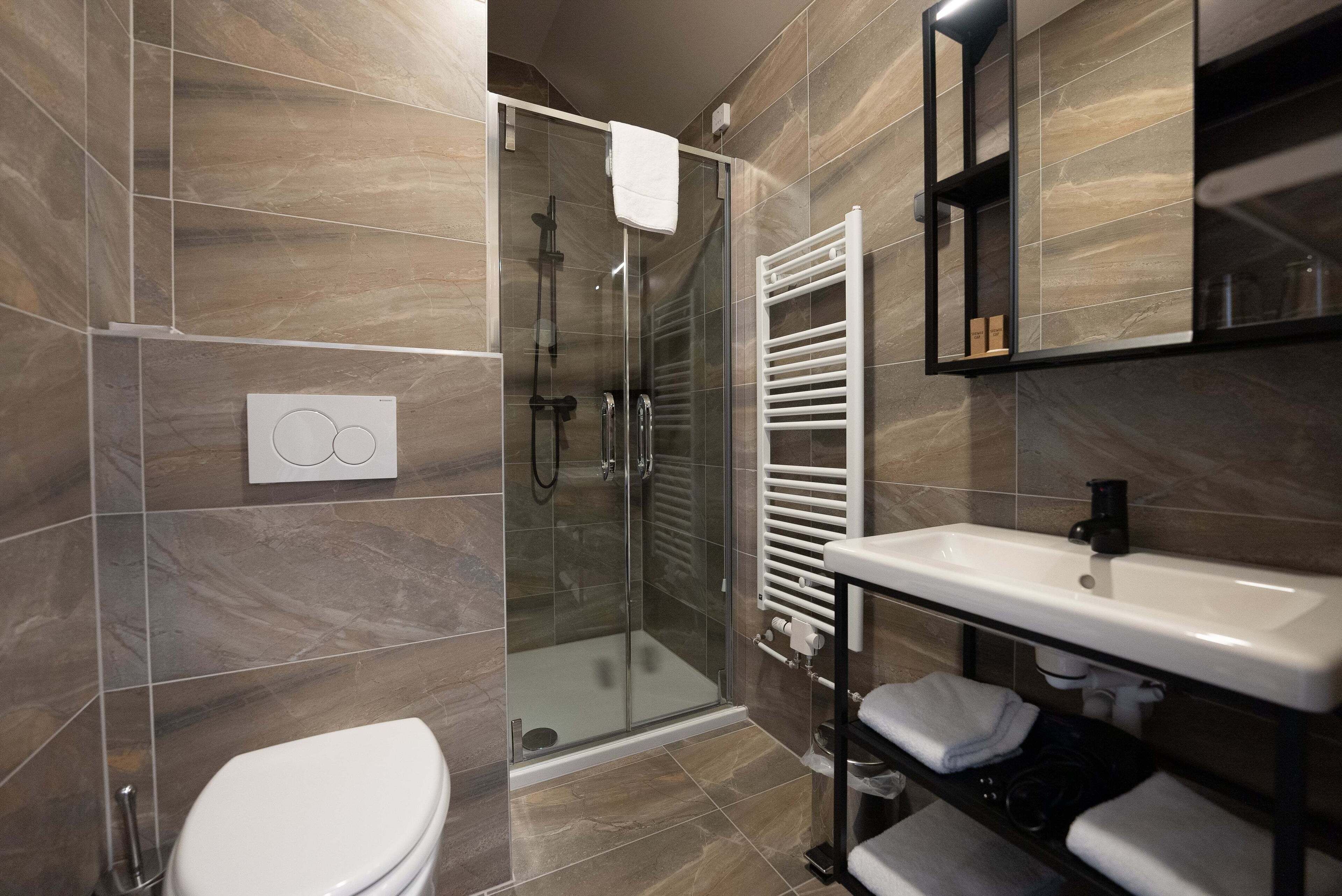 A modern bathroom with a glass shower enclosure, a white toilet, a built-in sink, and a towel rack.