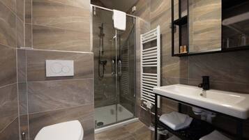 A modern bathroom with a glass shower enclosure, a white toilet, a built-in sink, and a towel rack.