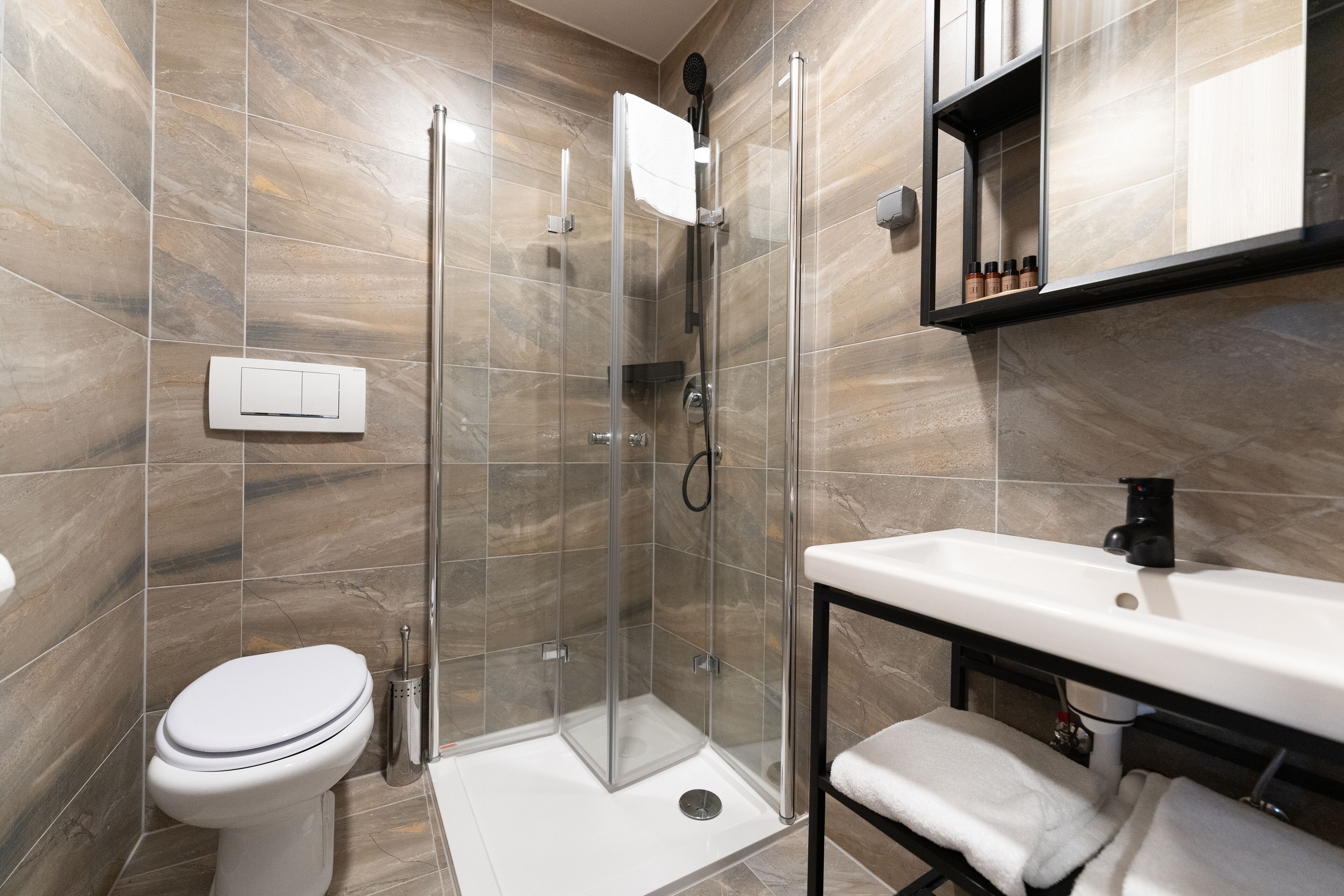 Un baño moderno con ducha envuelta en vidrio, inodoro blanco y lavamanos con grifo negro.