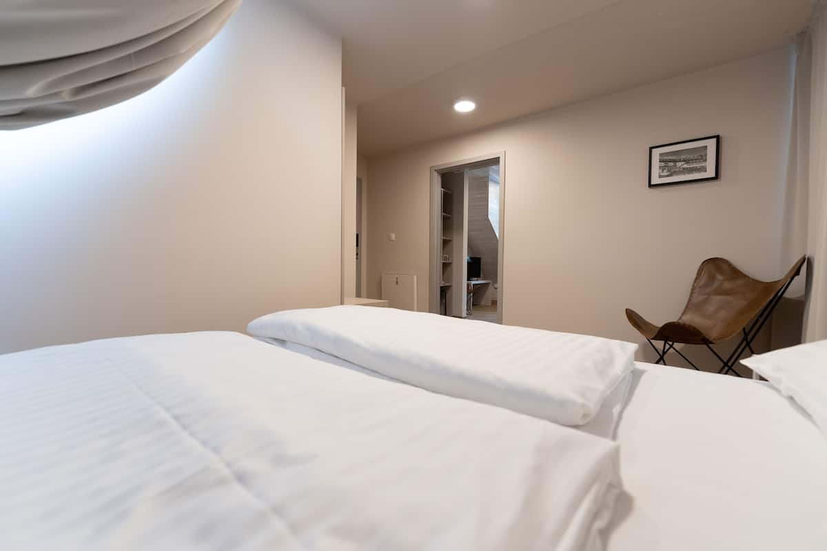 A hotel room with two beds, a chair, a wardrobe, and a framed picture on the wall.