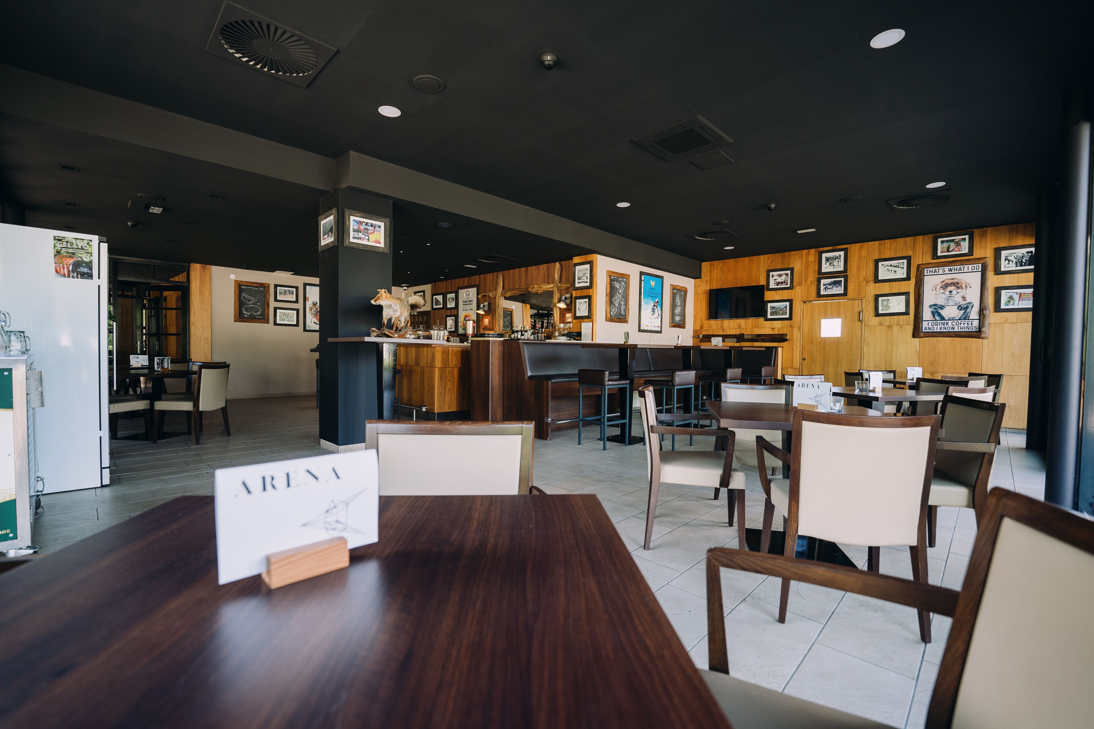 A restaurant with wooden tables and chairs, a bar area, and framed pictures on the walls.