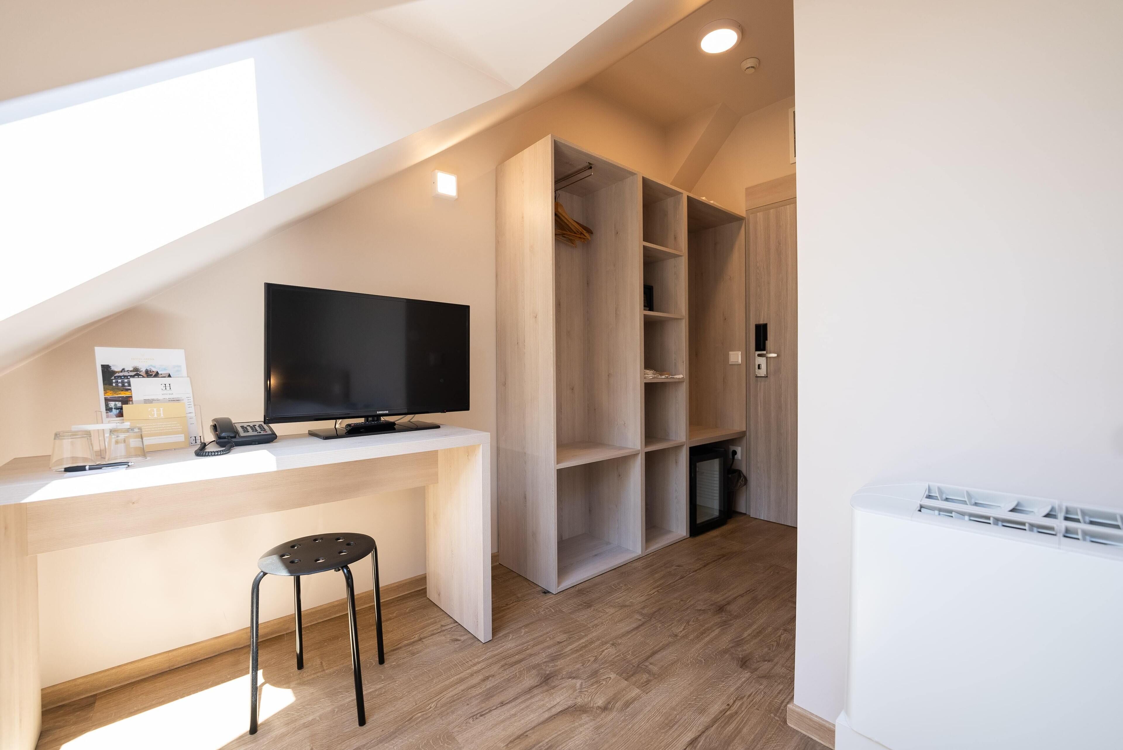 A modern, well-lit room with a wooden desk, a black chair, a TV, and a walk-in closet.