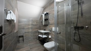 Une salle de bain moderne avec une douche à parois de verre, des toilettes blanches, un lavabo avec un miroir et un petit tabouret.
