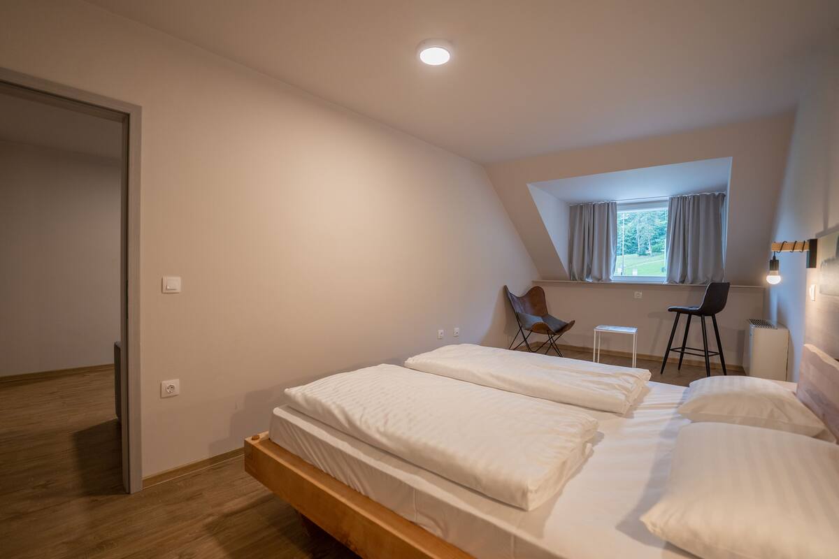 A bedroom with a loft-style bed, a desk, and a window with curtains.