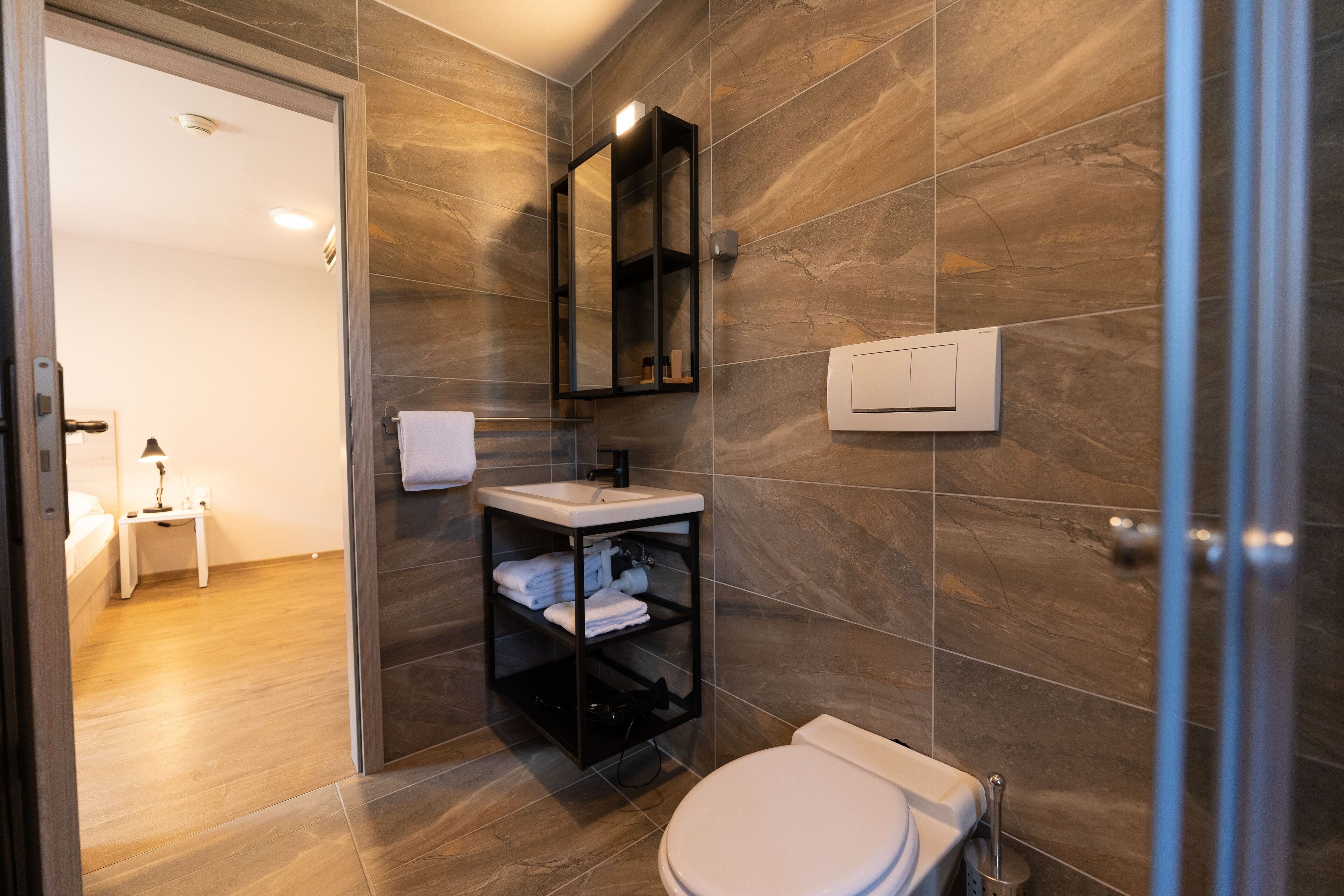 Un baño moderno con inodoro blanco, tocador negro con espejo y un perchero.