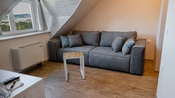 A modern living room with a grey sofa, a small wooden table, and a view through a window.