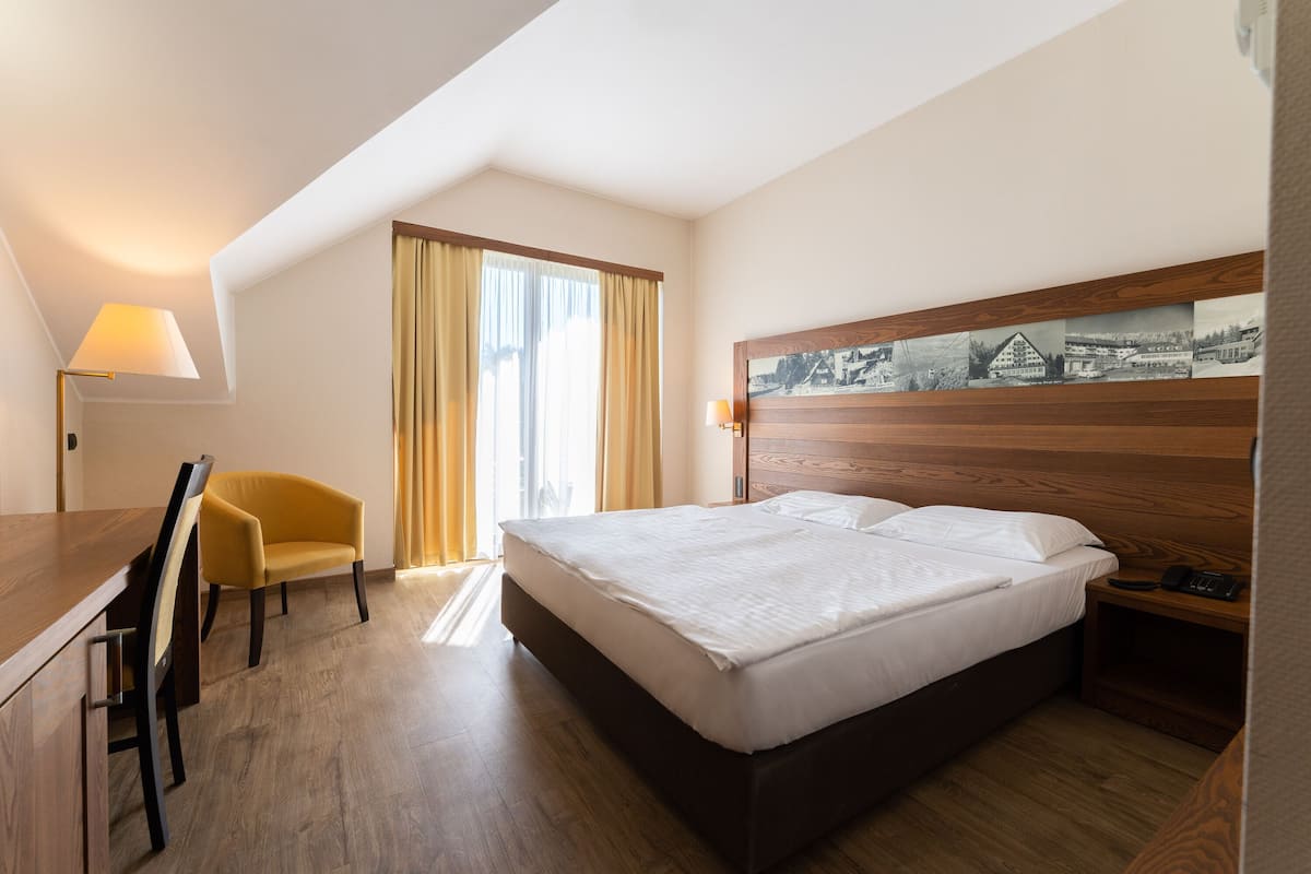A hotel room with a large bed, a desk, a chair, a lamp, and a wall-mounted artwork.