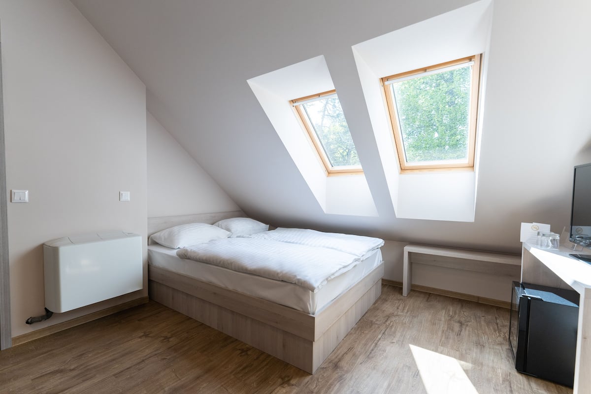 A bedroom with a sloped ceiling, skylights, a bed, a desk, and a radiator.
