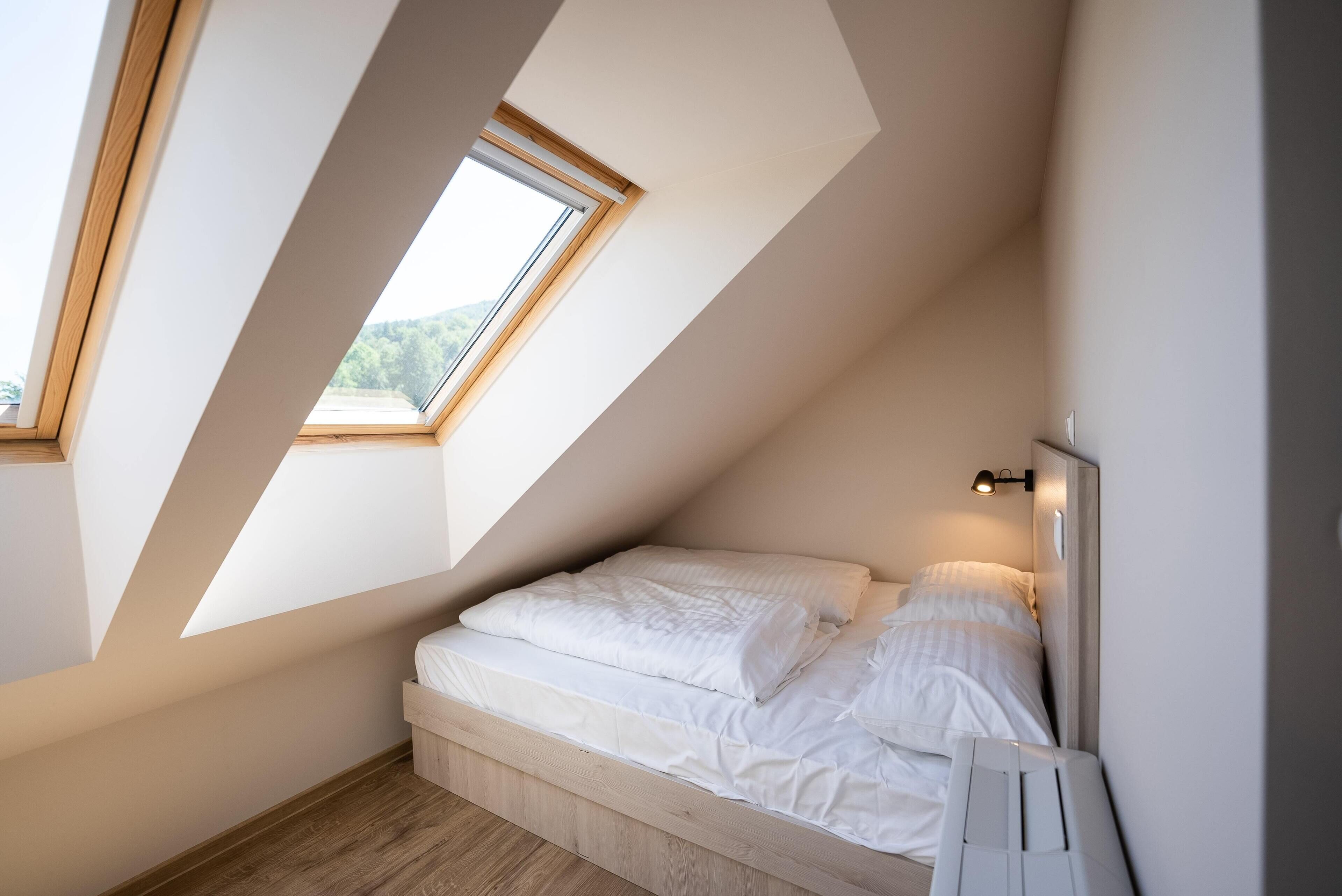 A small, modern bedroom with a sloped ceiling and a skylight, providing natural light.