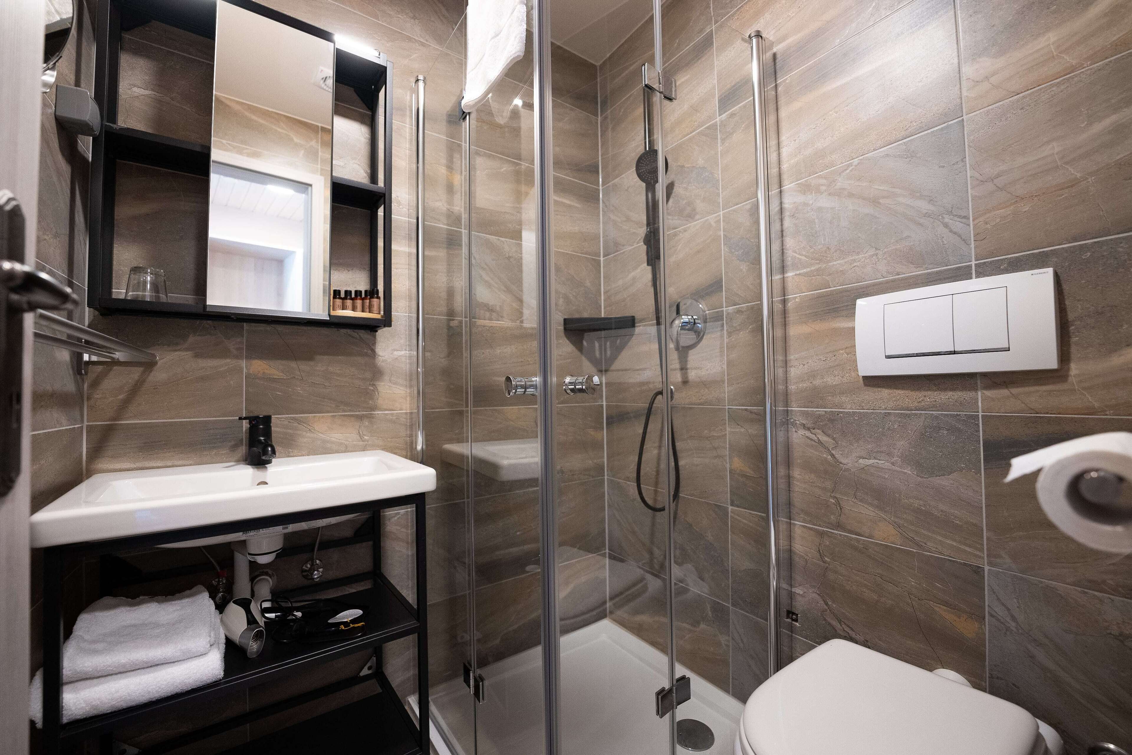 Et moderne badeværelse med en glasafskærmet brusekabine, en hvid vask og et toilet.