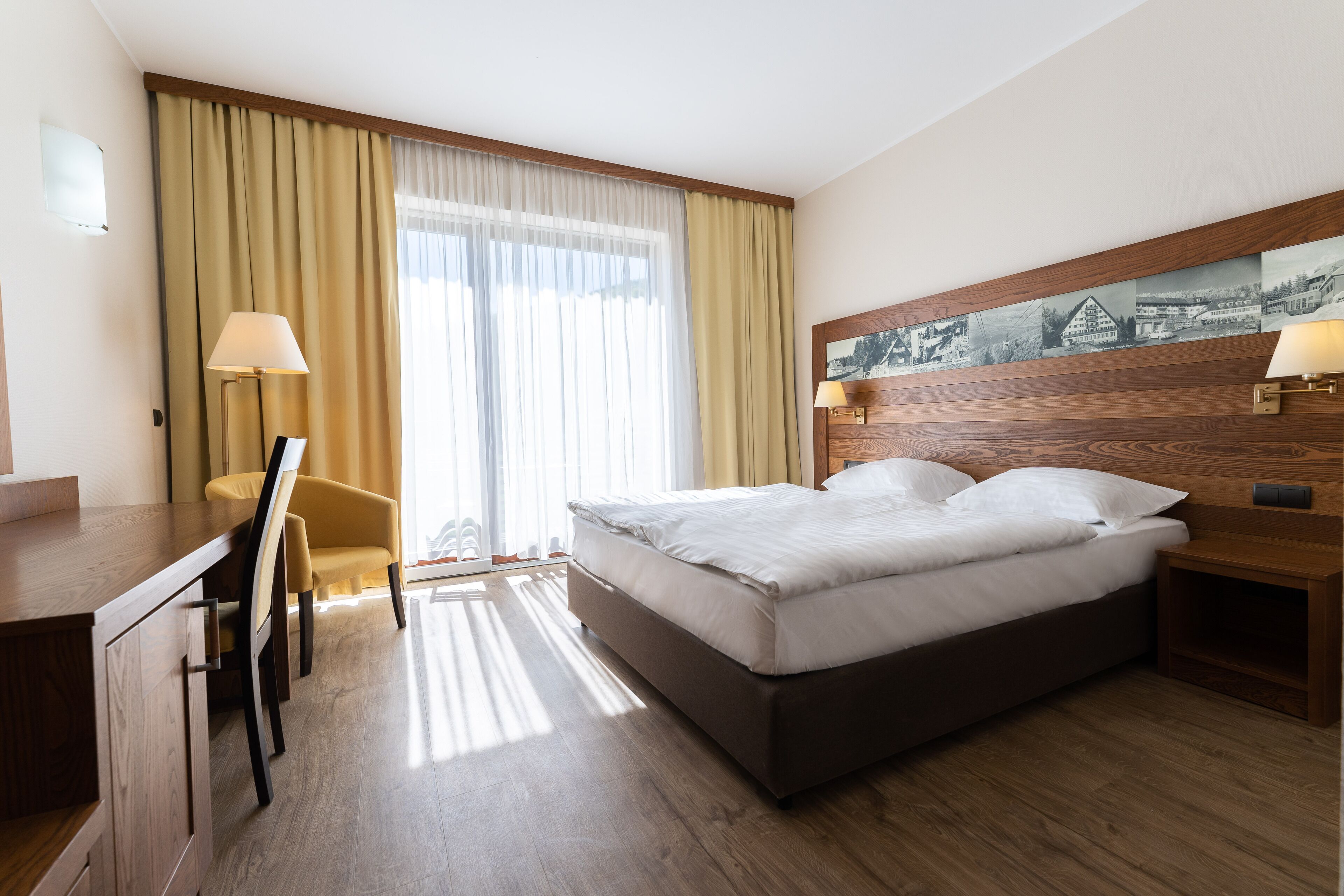 Una habitación de hotel con cama, escritorio, silla y ventana con cortinas.