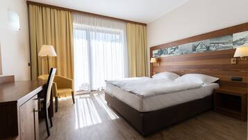 Una habitación de hotel con cama, escritorio, silla y ventana con cortinas.