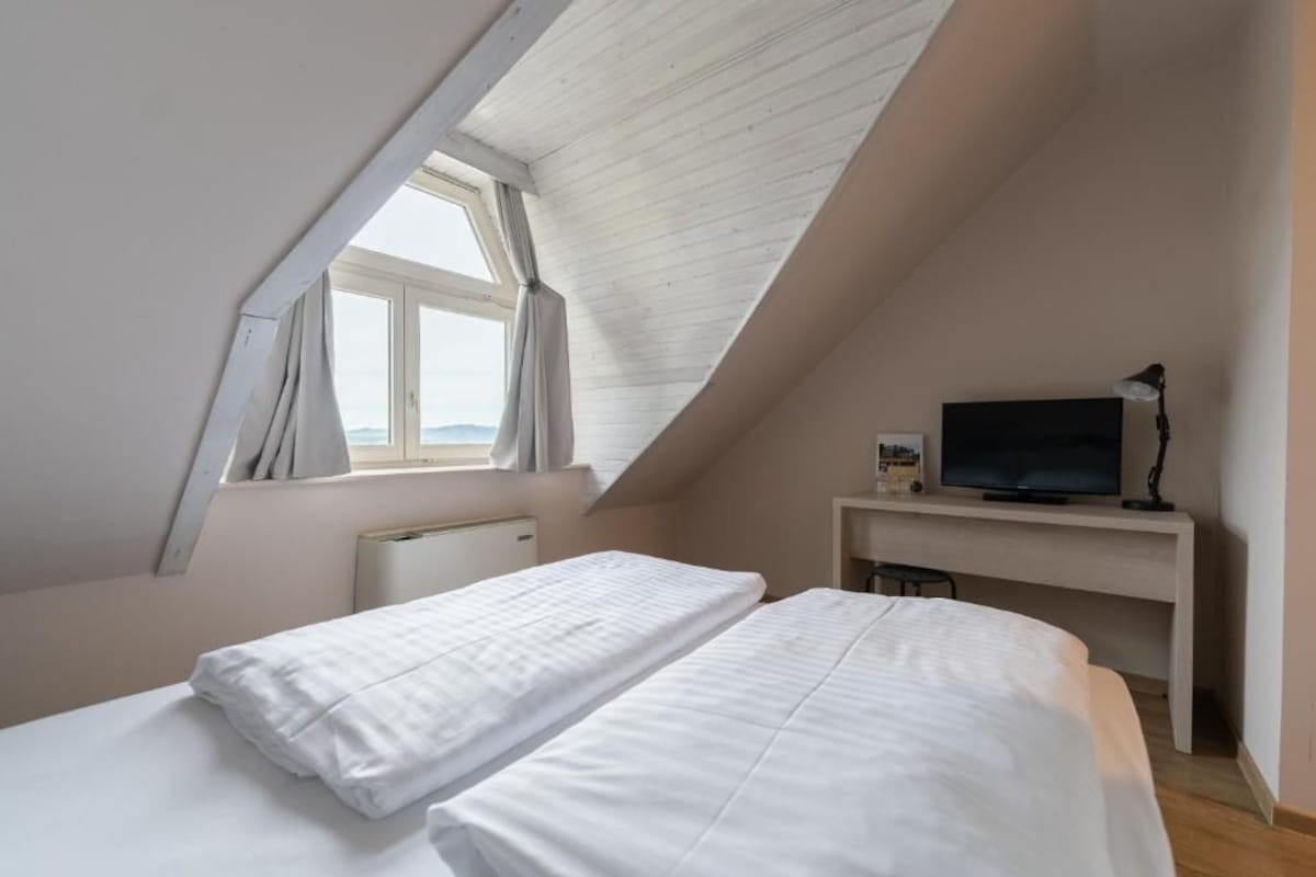 A bedroom with two beds, a desk with a TV, and a window with curtains.