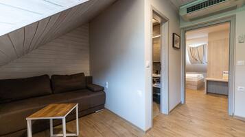 Un espace de vie moderne et compact, doté d’un plafond en pente, d’un plancher en bois, d’un canapé marron et d’une petite table blanche.