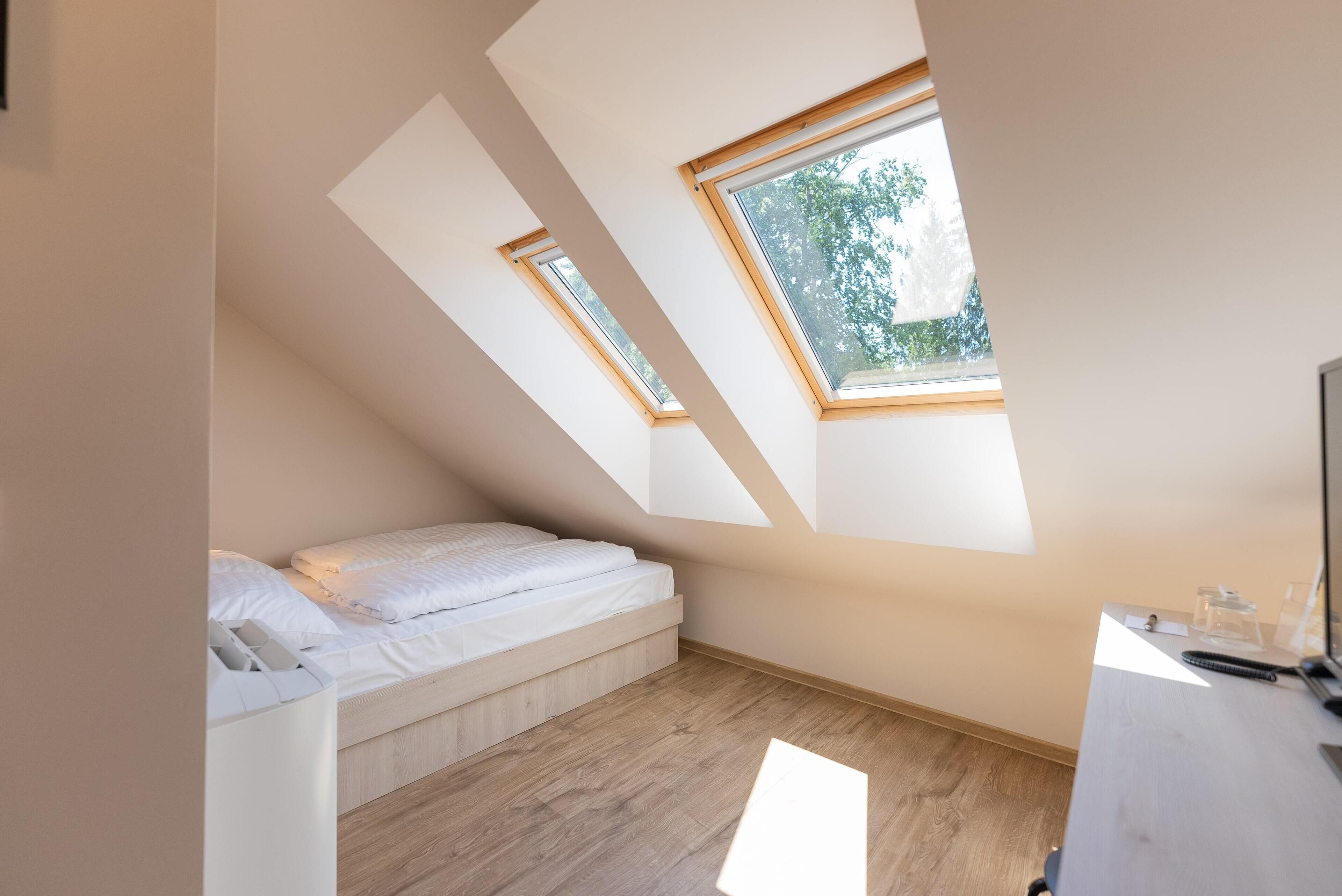 Ein kleines, modernes Schlafzimmer mit schrägem Dach, Dachfenstern, einem Bett und einem Schreibtisch.