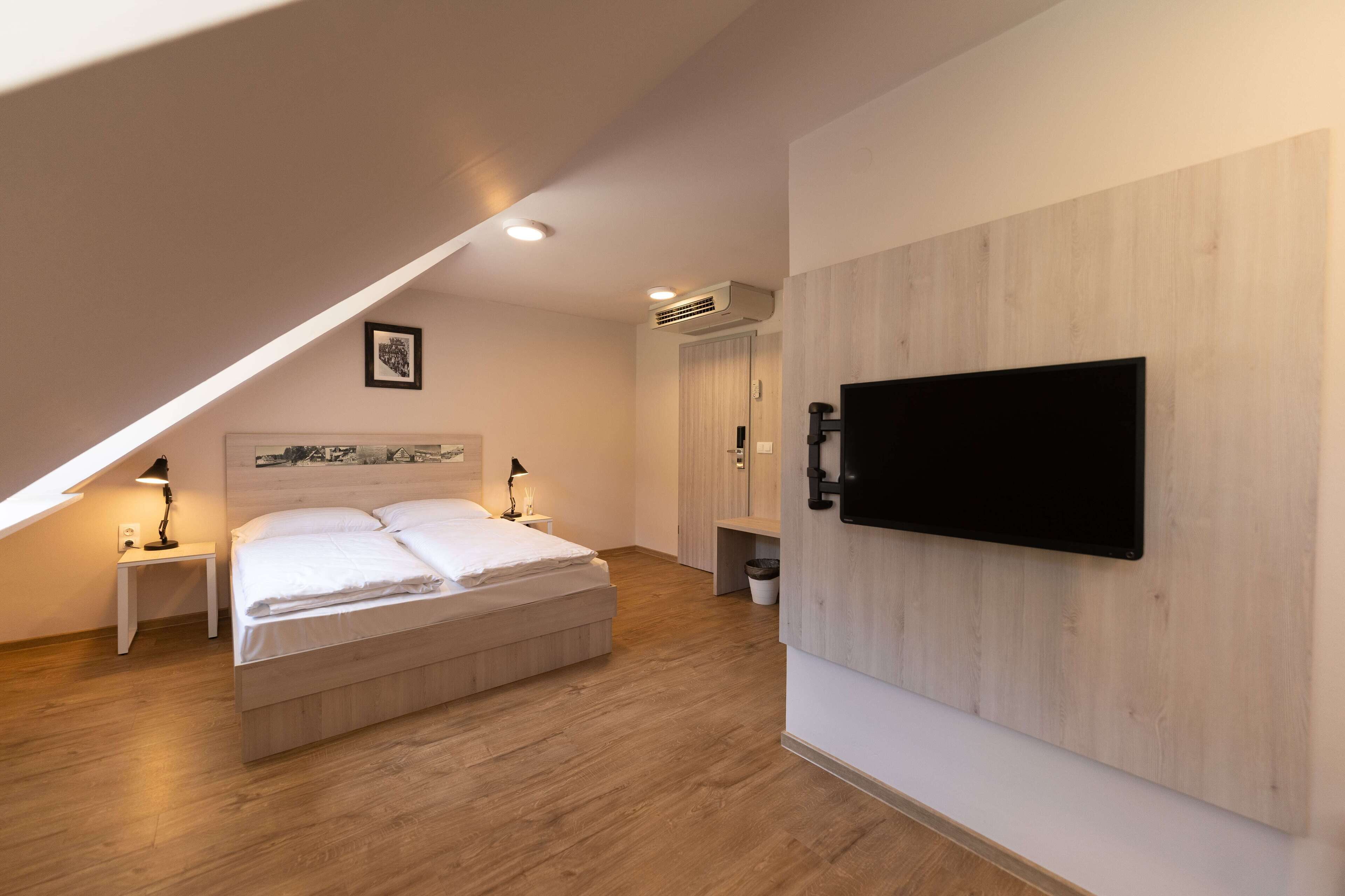 A bedroom with a bed, bedside lamps, a mounted TV, and a ceiling fan.