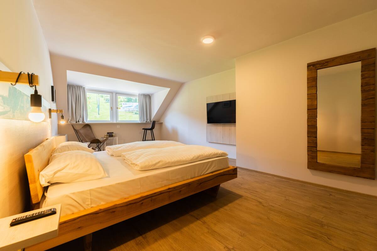 A modern bedroom with a wooden bed, a TV mounted on the wall, and a large mirror.