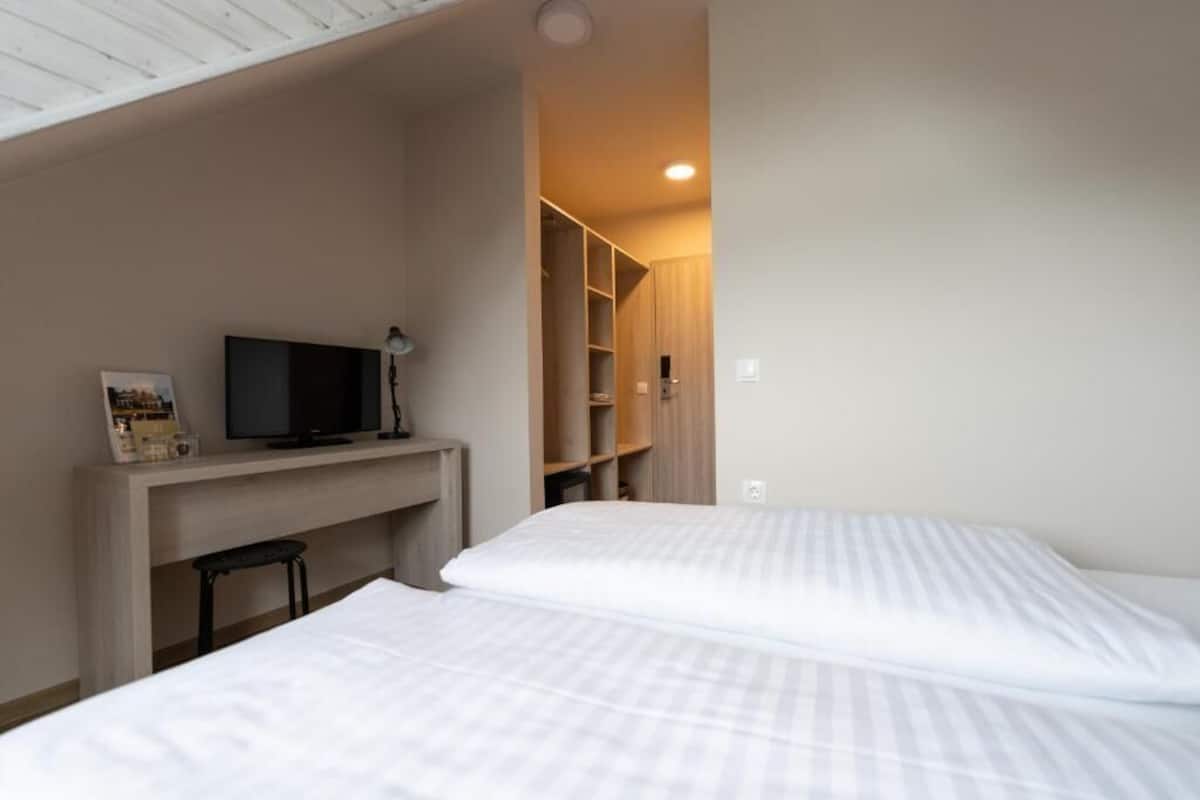 A bedroom with a bed, a desk with a television, and a closet.