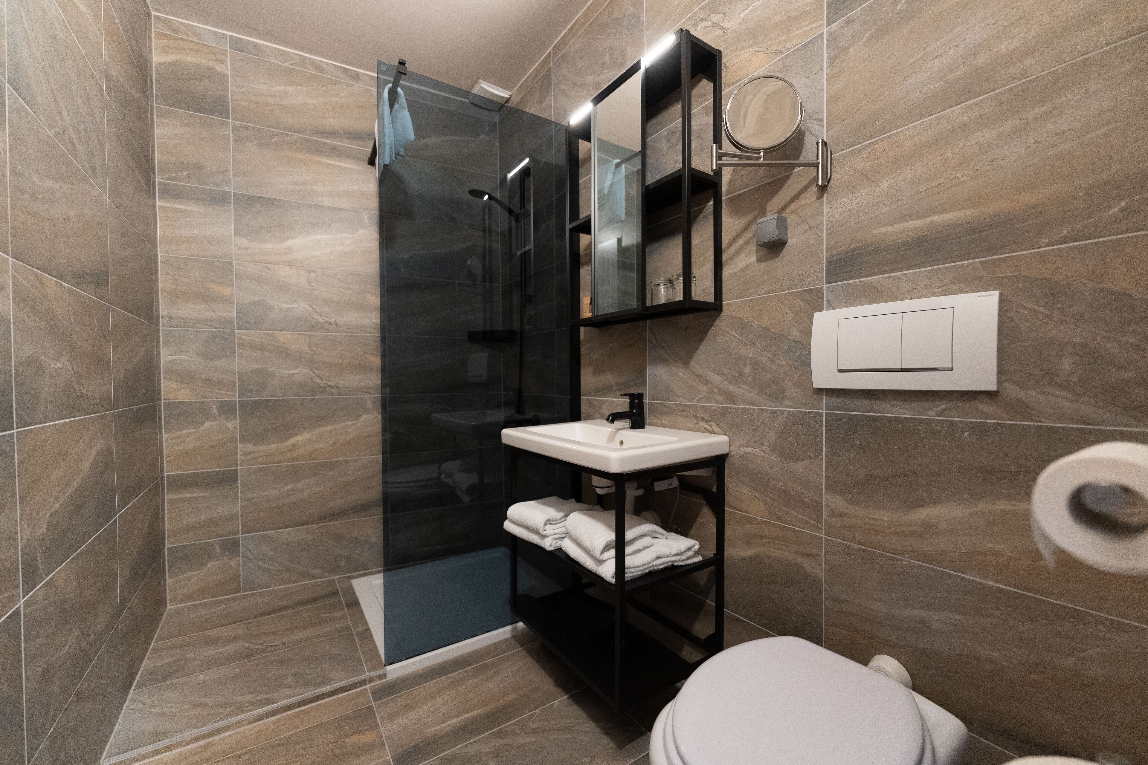 Un baño moderno con ducha envuelta en vidrio, un lavamanos blanco y un inodoro.