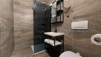 Un baño moderno con ducha envuelta en vidrio, un lavamanos blanco y un inodoro.
