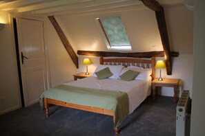 A bedroom with a sloped ceiling, a bed with green bedding, two bedside lamps, and a radiator. - Large manor house for rent in Normandy, a stone's throw from Suisse Normande! (fresné-la-mère)