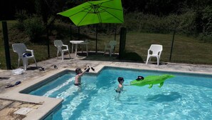 Een zwembad met een groene opblaasbare krokodil, witte stoelen en een groene parasol.