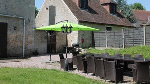 Een gebouw van steen met een schuin dak, een tafel met stoelen en een groene parasol.