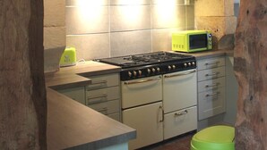Een landelijke keuken met een fornuis, magnetron en een klok aan de muur.