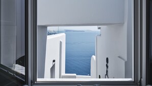 A view through a window of a room with white walls and a view of the sea.
