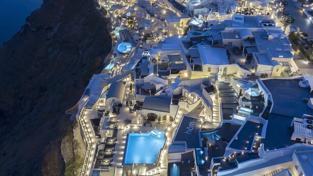 An aerial view of a coastal hotel with multiple swimming pools, a large central pool, and a rocky coastline.