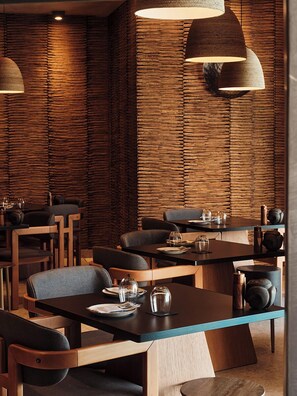 A modern restaurant interior with wooden panel walls, dark tables, and chairs. - Hom Santorini (Santorini)