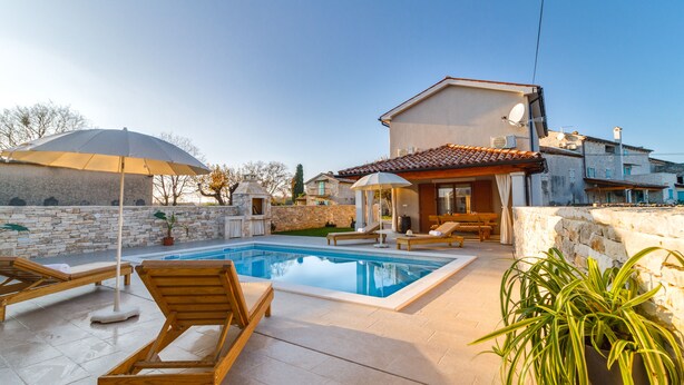 A poolside area with lounge chairs, a swimming pool, and a house with a tiled roof. - Romantic Istrian Villa Nima with private pool (Glavani)